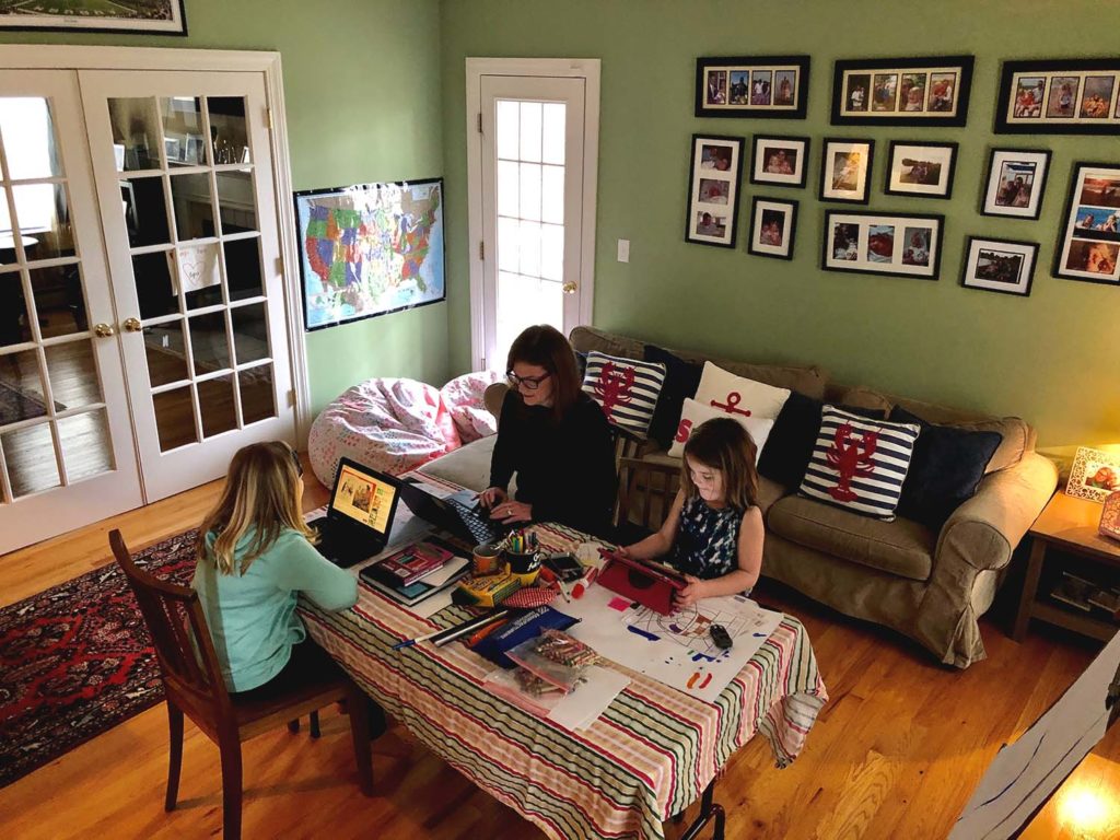 Woman and two girls in a living room all on computers at a table.