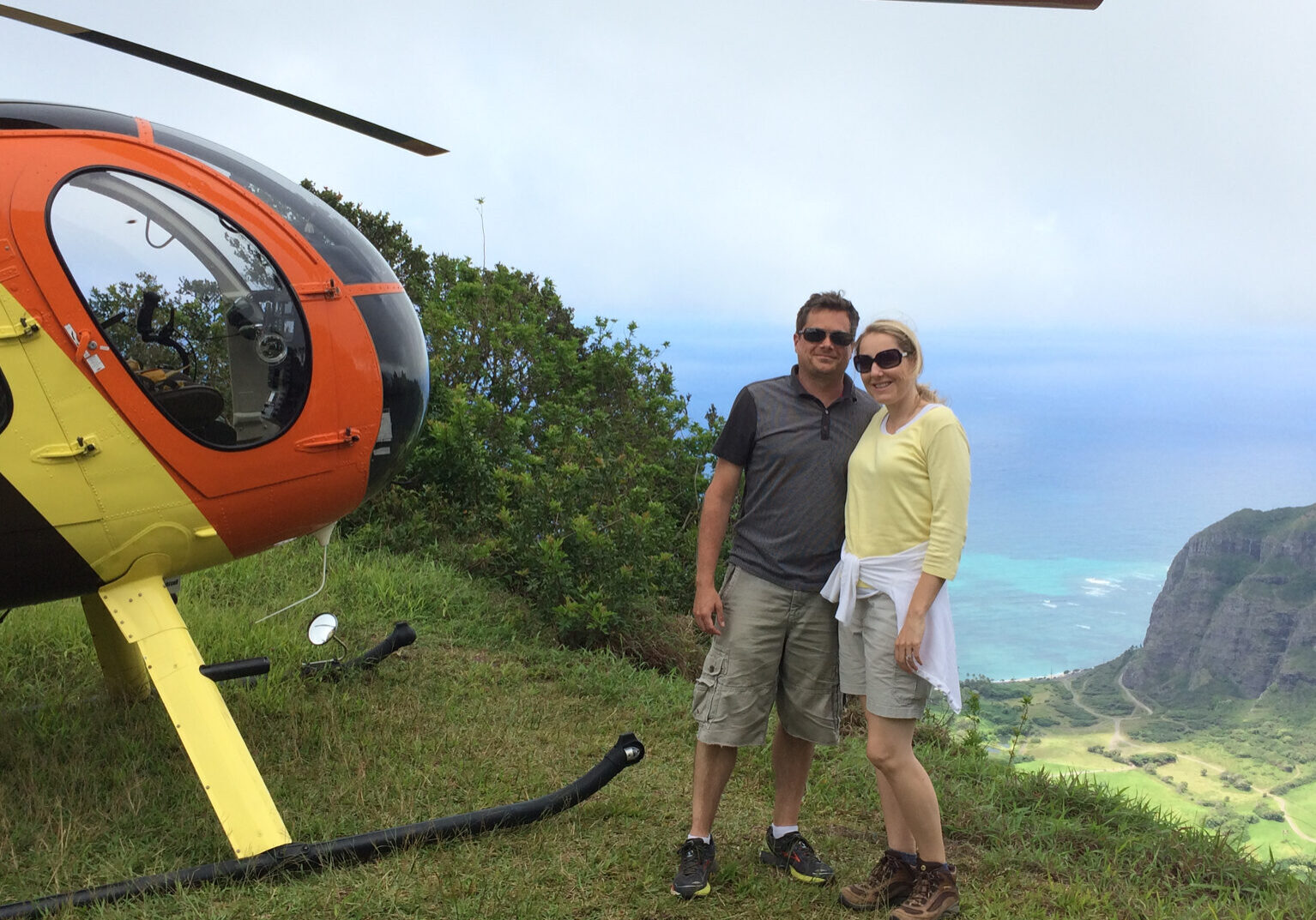 Man and woman on a mountain by a helicopter.