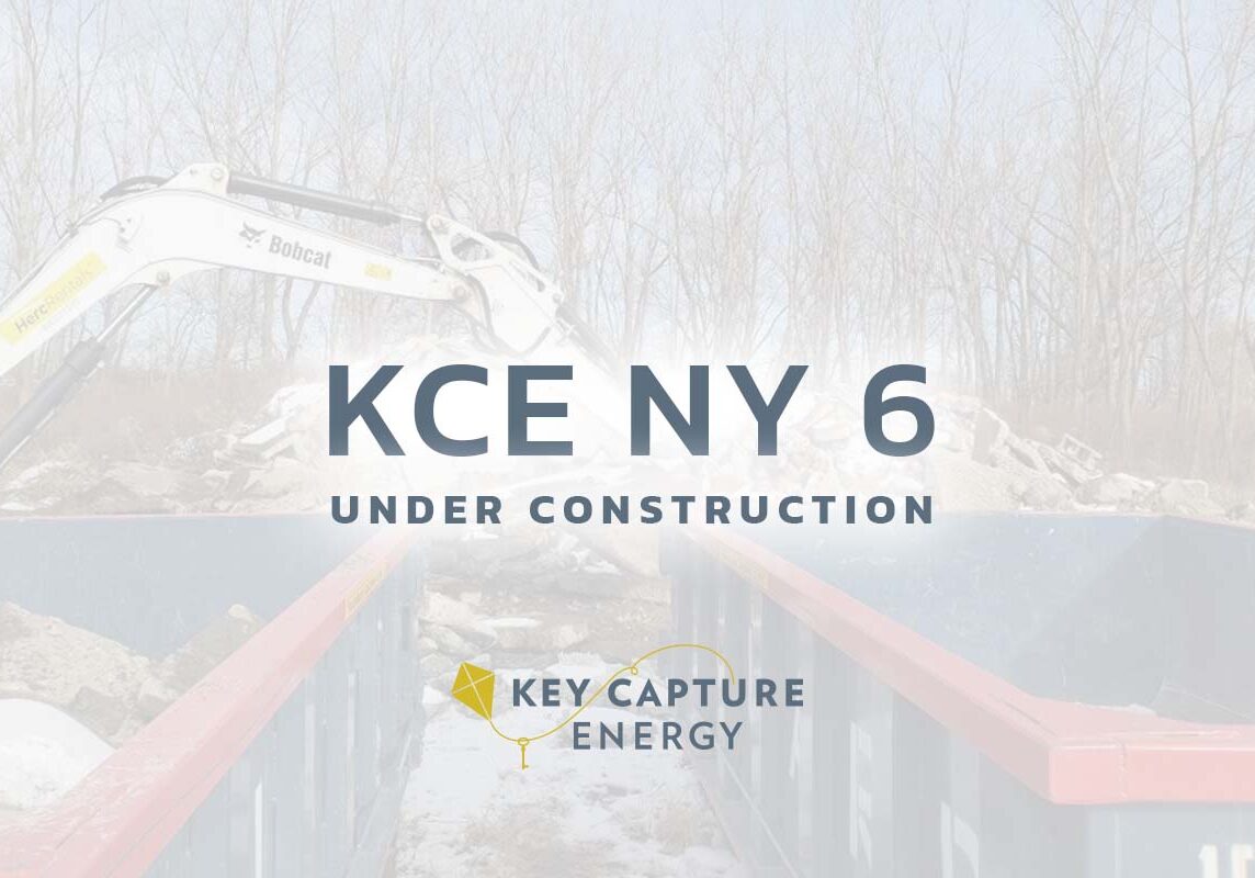 The words KCE NY 6 under construction with Key Capture Energy logo underneath it, construction site behind.